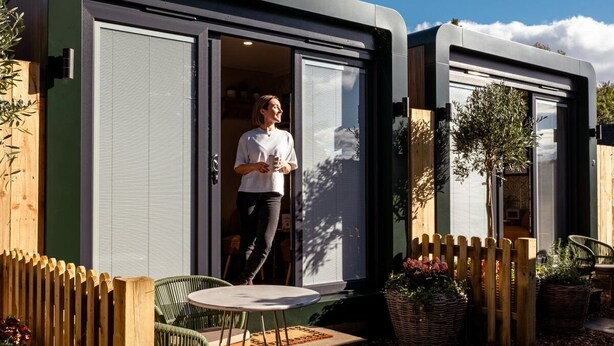 A modern, compact mobile home with a sliding door, a small patio with a table and chairs, and a wooden fence. - High Corner Inn (Ringwood)