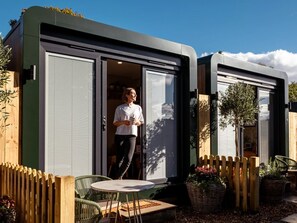 Una casa móvil moderna y compacta con puerta corredera, un pequeño patio con mesa y sillas, y una valla de madera.