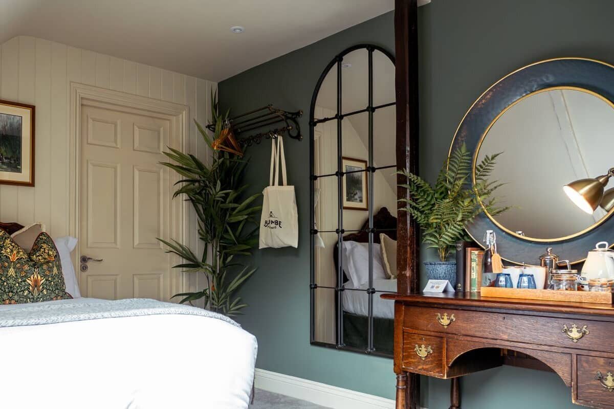 A bedroom with a bed, a dresser with a mirror, a plant, and a door.
