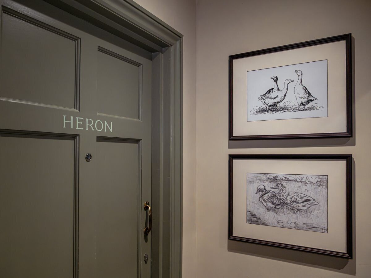Un pasillo con una puerta que dice "HERON" y dos dibujos en blanco y negro enmarcados en la pared.