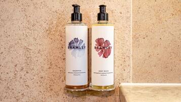 Twee flessen Bramble shampoo en douchegel op een beige betegelde muur.