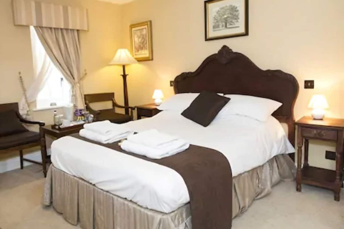 A neatly made bed with a brown headboard, a bedside lamp, and a framed picture on the wall.