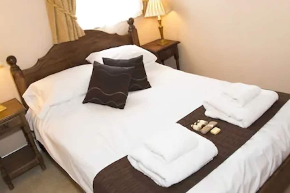 A neatly made bed with pillows, a folded towel, and toiletries on the bed.