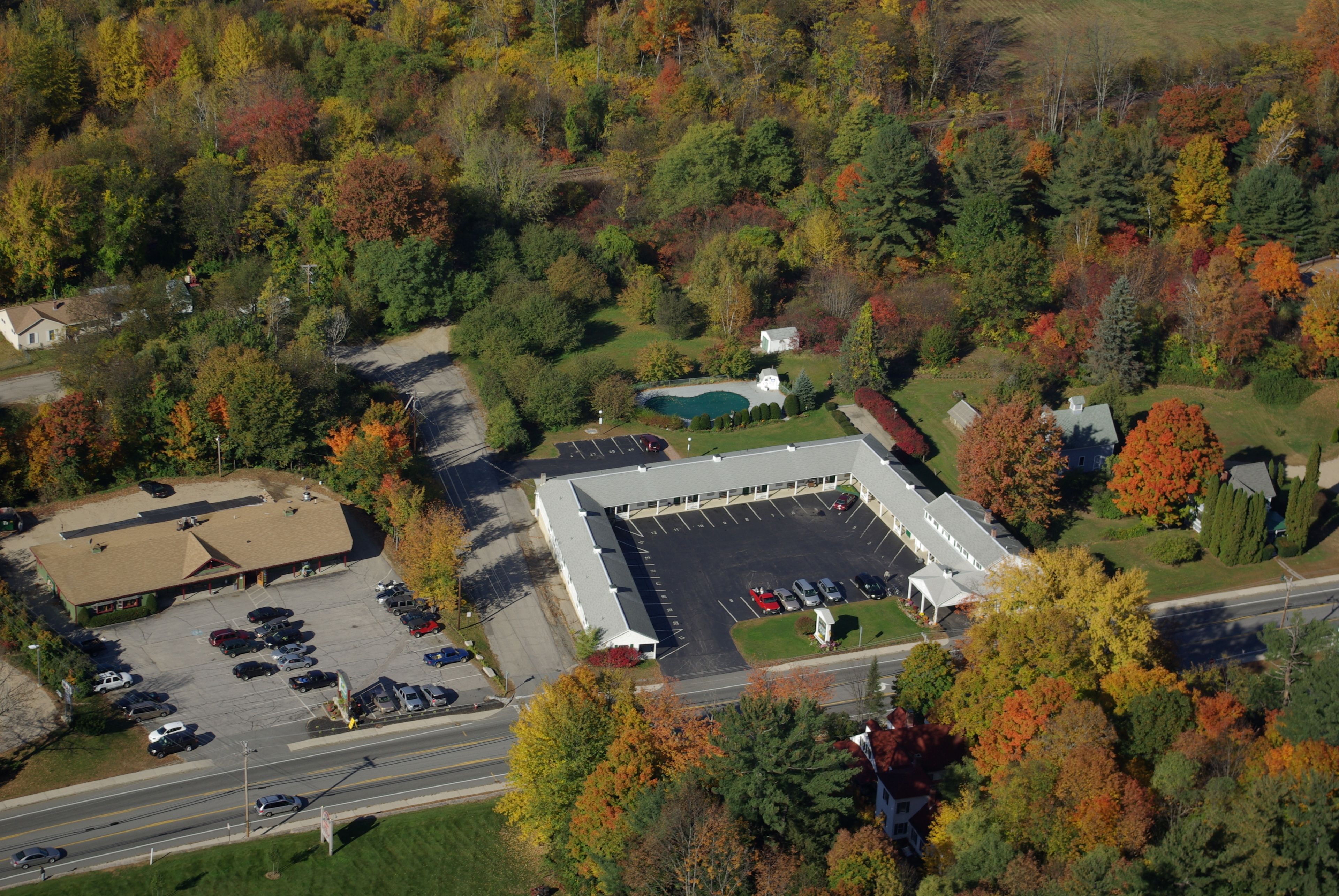 An aerial view of a commercial building with a parking lot, surrounded by autumn-colored trees.