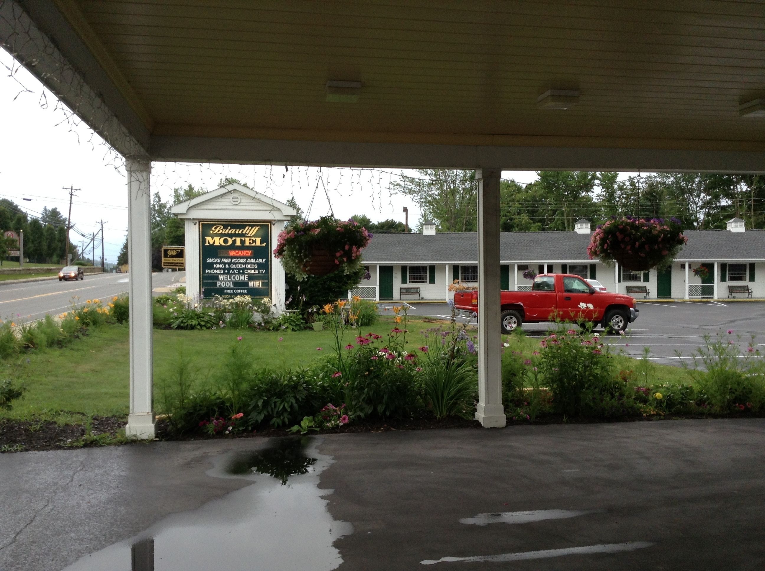 A motel with a covered parking area, a signboard, and a red car parked in front.