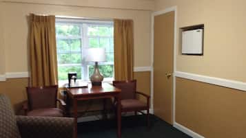 Habitación de hotel con zona de comedor que incluye una mesa, sillas, una lámpara y un ventanal con cortinas.