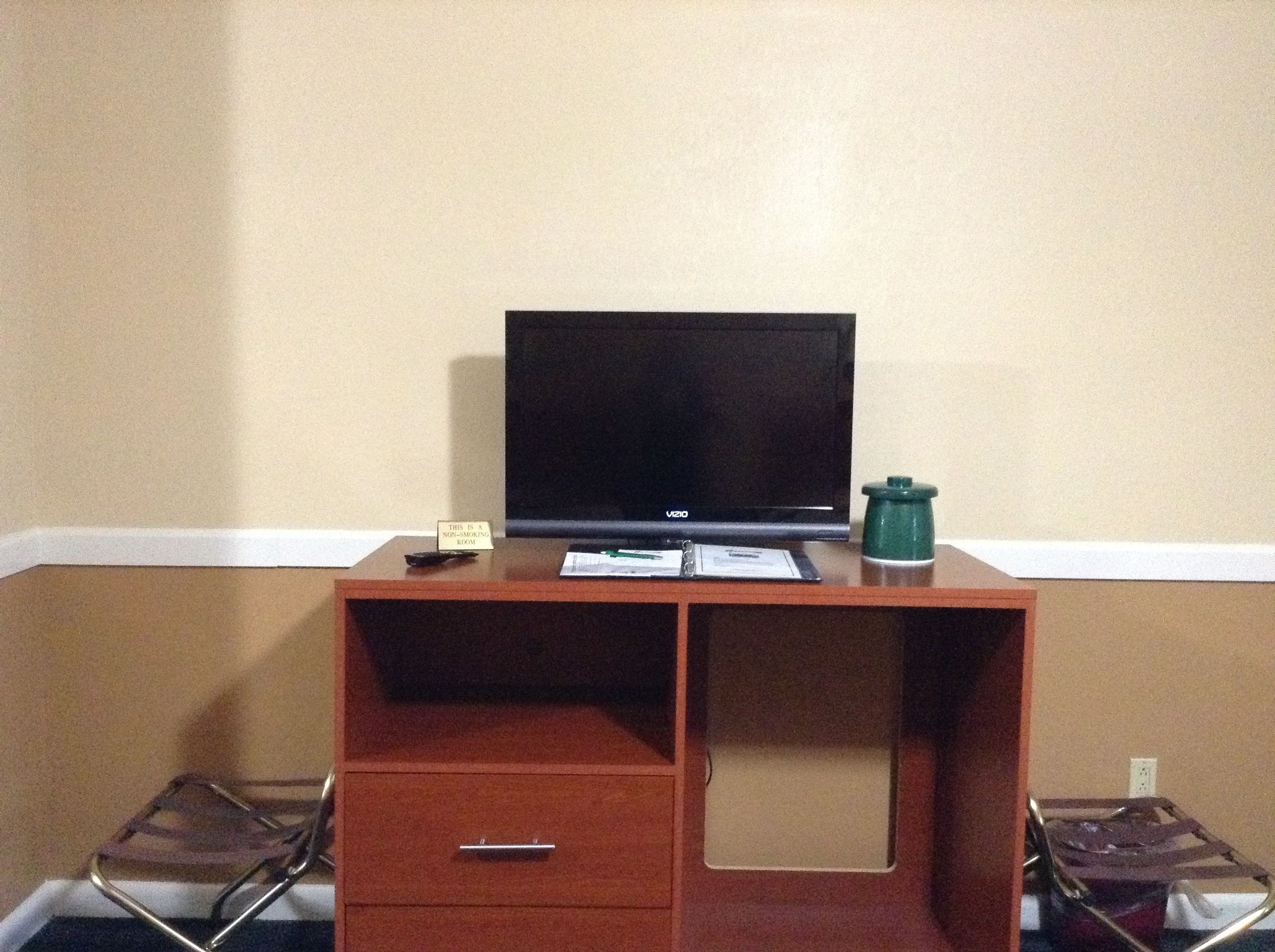 A small desk with a television, a nameplate, a green container, and a pair of chairs.