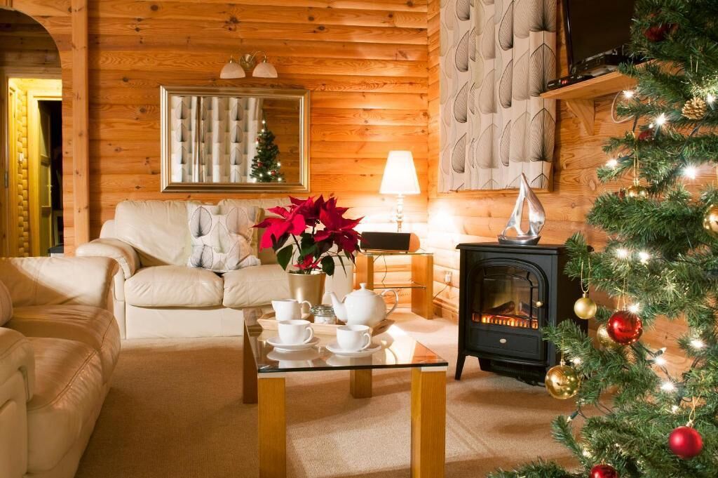 A cozy log cabin interior with a fireplace, a Christmas tree, and a sofa.