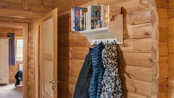 A wooden interior with a bookshelf holding books and a coat rack with jackets.