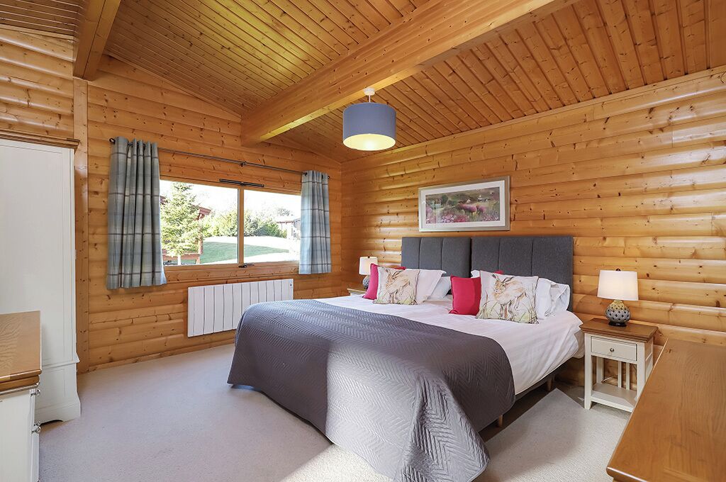 A wooden-paneled bedroom with a bed, bedside tables, a window with curtains, and a ceiling light.