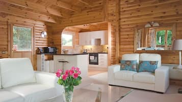 A wooden cabin interior with a living area, kitchen, and a dining table.