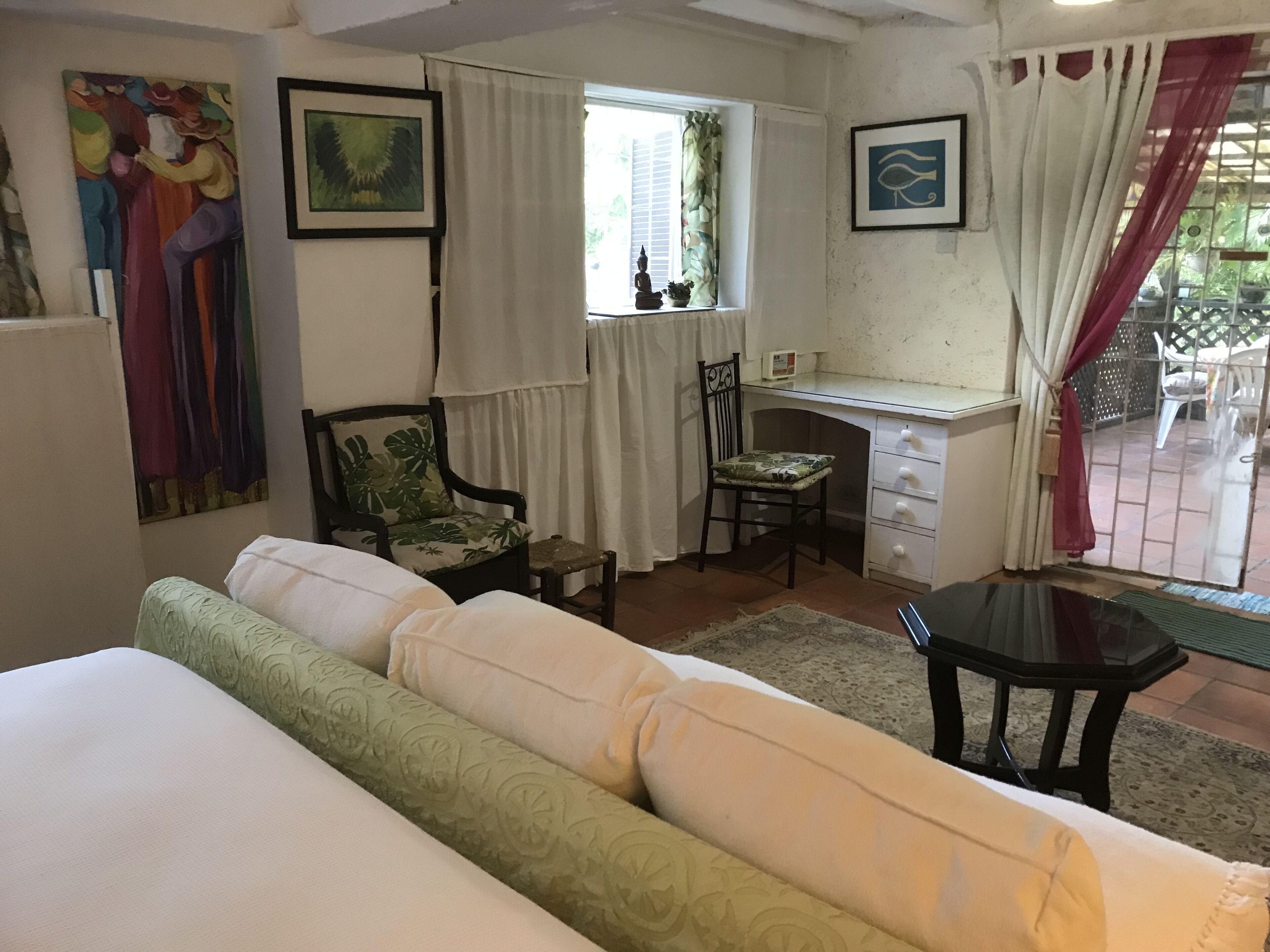 A room with a bed, a desk, a chair, and a sofa. There are curtains, a window, and artwork on the walls.