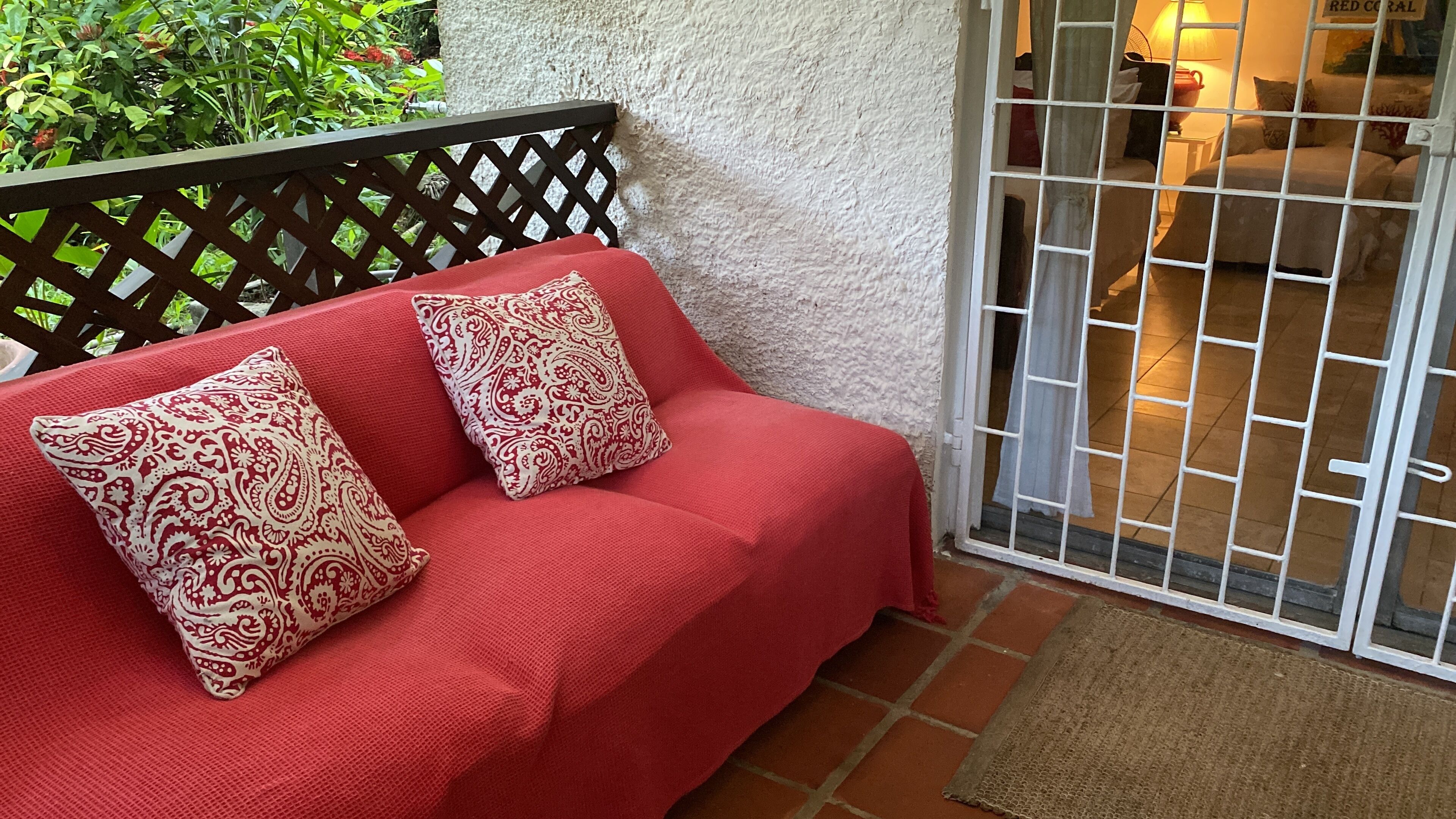 A red sofa with patterned cushions, a wooden lattice, and a white textured wall.