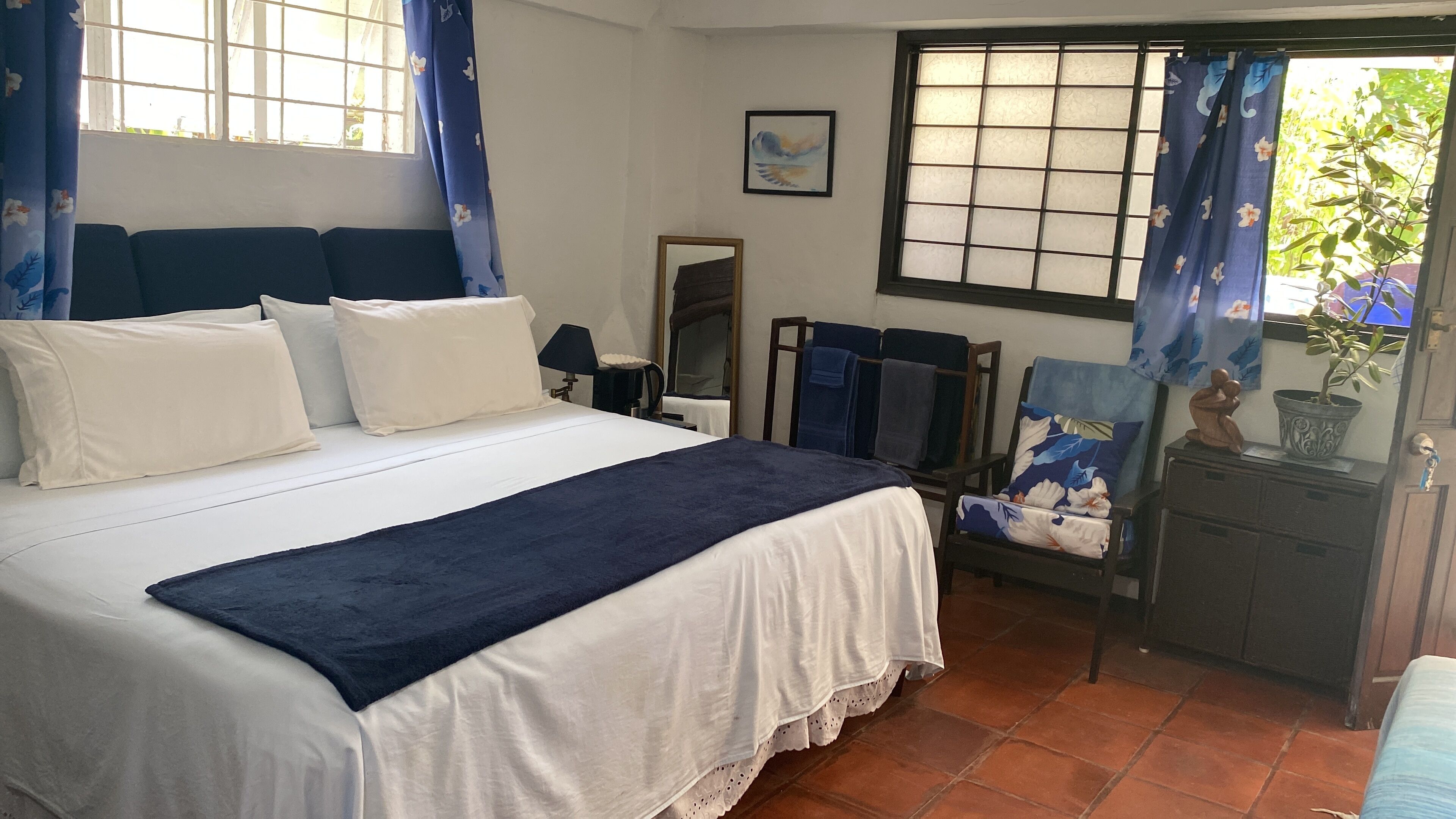 A neatly arranged hotel room with a bed, a chair, a small table with a plant, and a window with curtains.