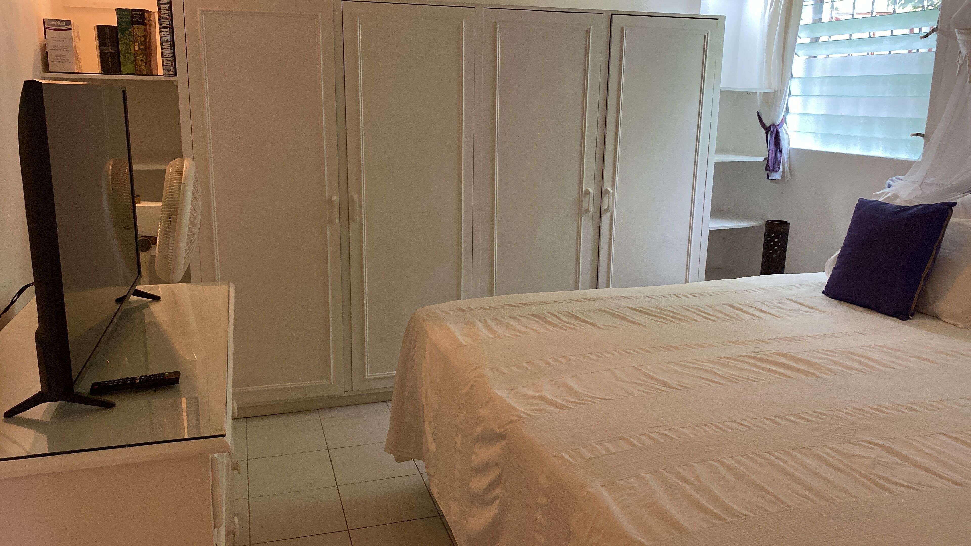Ein Schlafzimmer mit Bett, Kleiderschrank, Schreibtisch und einem Fenster mit Jalousien.