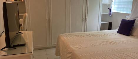 Ein Schlafzimmer mit Bett, Kleiderschrank, Schreibtisch und einem Fenster mit Jalousien.