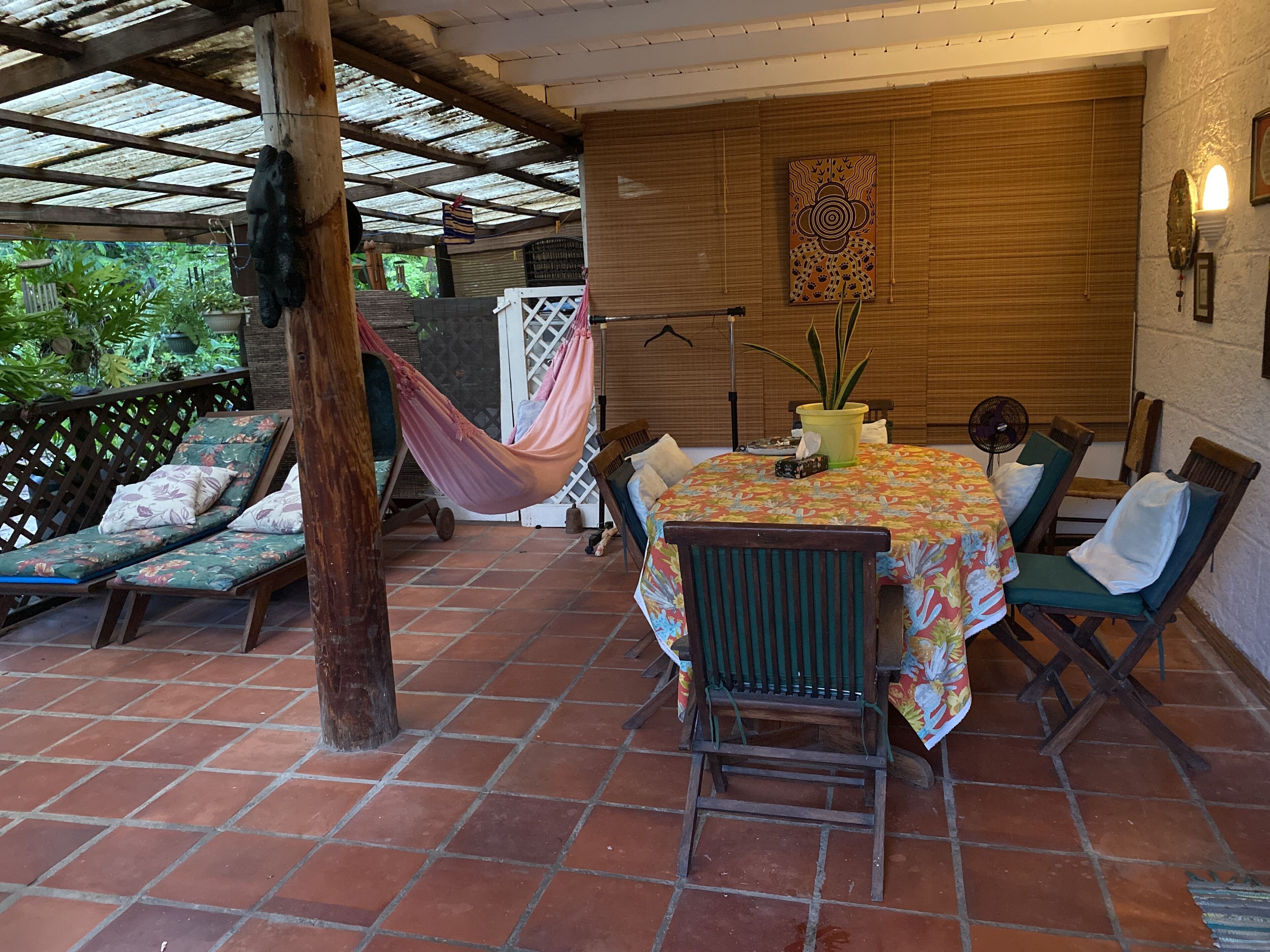 Een overdekt terras met een tafel, stoelen, een hangmat en een houten wand met een decoratief paneel.