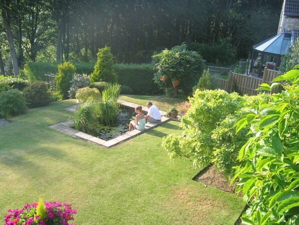 A well-maintained garden with a pond, seating area, and various plants. - Spinneycross (Corsham)