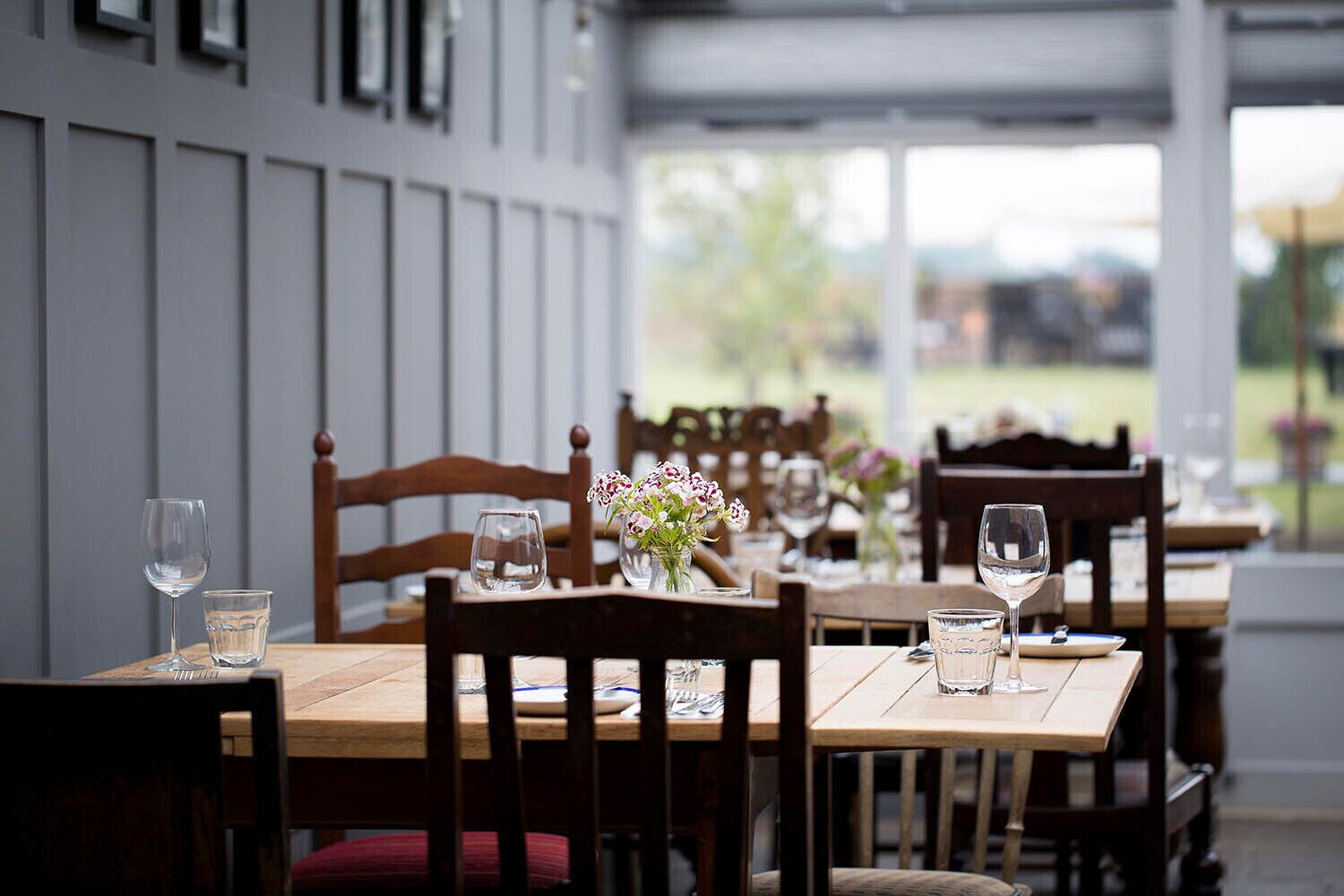 A restaurant with wooden tables and chairs, some with floral centerpieces.