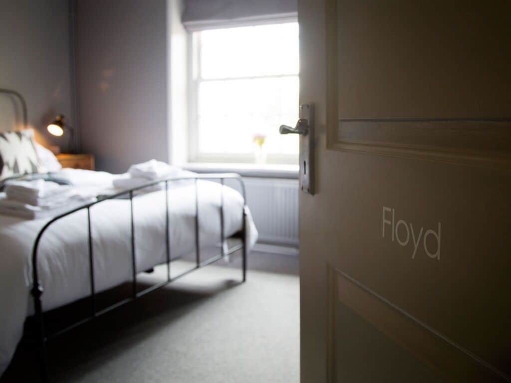 A bedroom with a bed, a bedside table with a lamp, a window with a view, and a door labeled "Floyd".