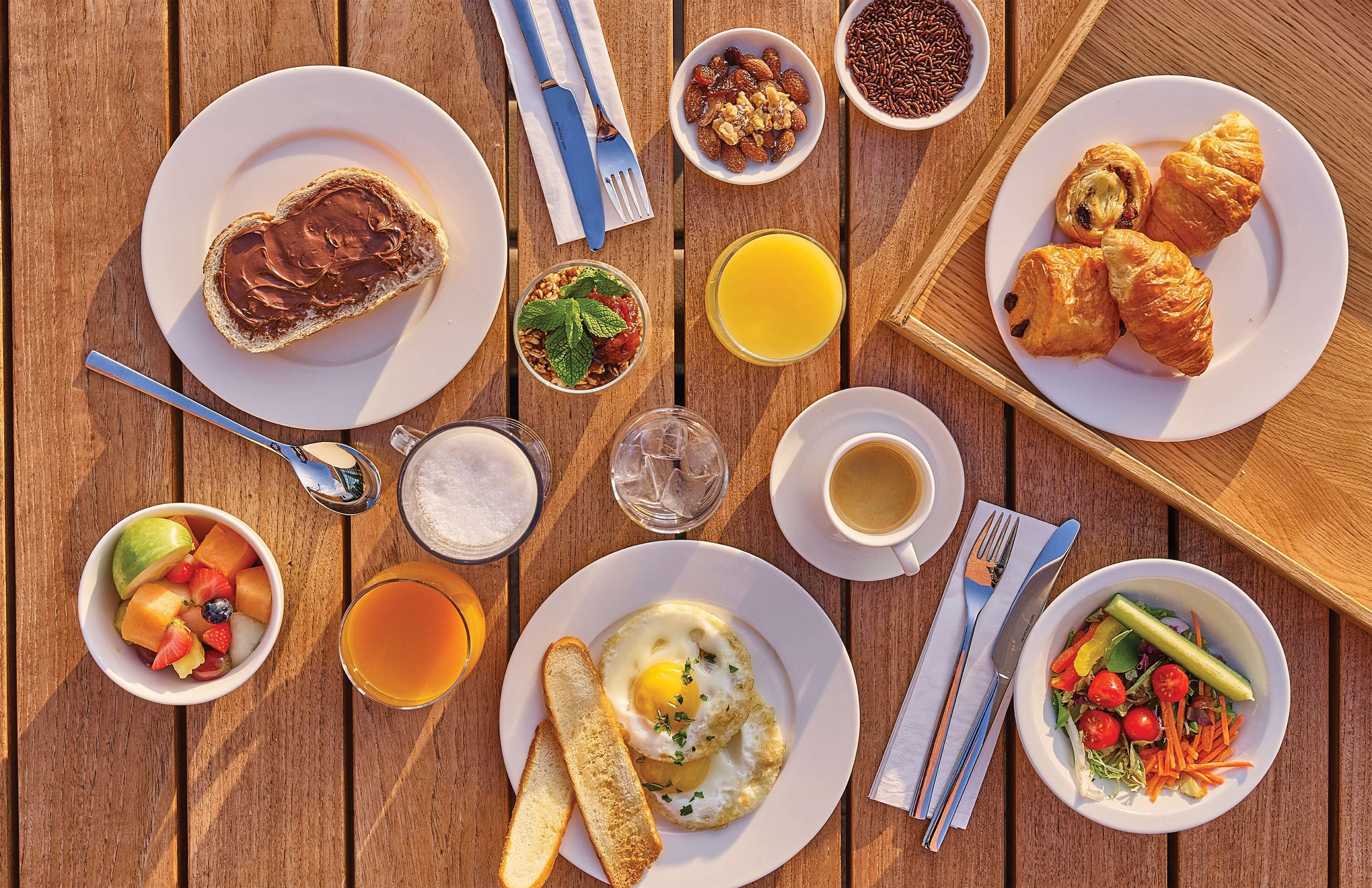 A breakfast table with various dishes including toast, eggs, fruit, and croissants.