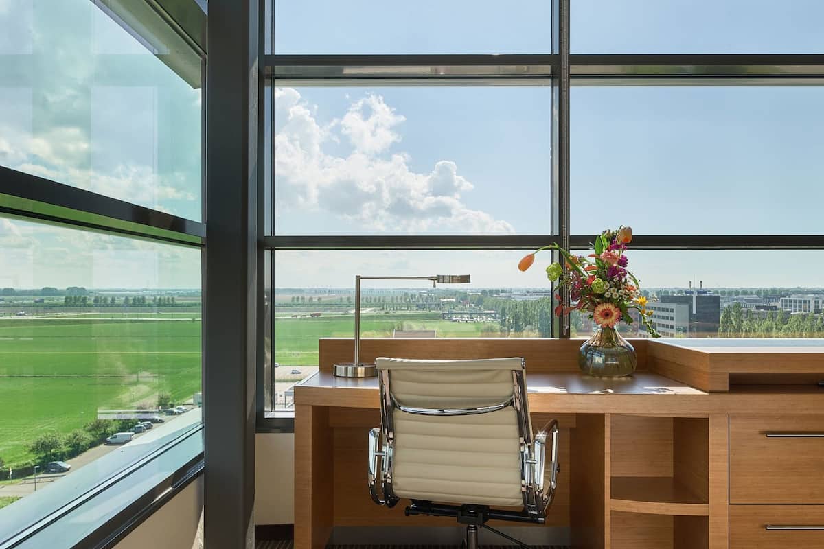 A modern office with a large window, a desk, a chair, and a vase of flowers.