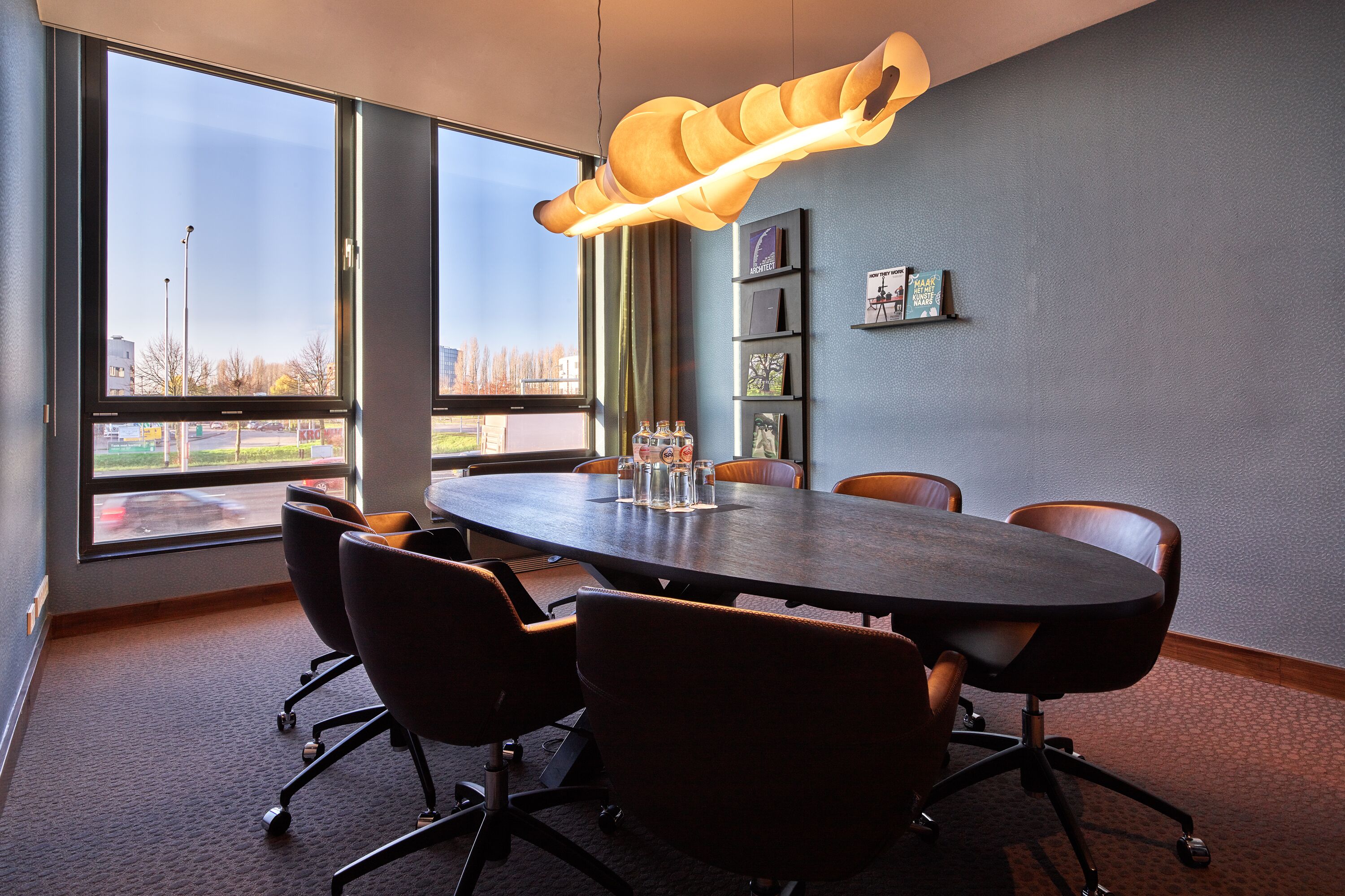 Une salle de conférence dotée d’une table ronde, de six chaises, d’une grande fenêtre et d’un luminaire suspendu original.