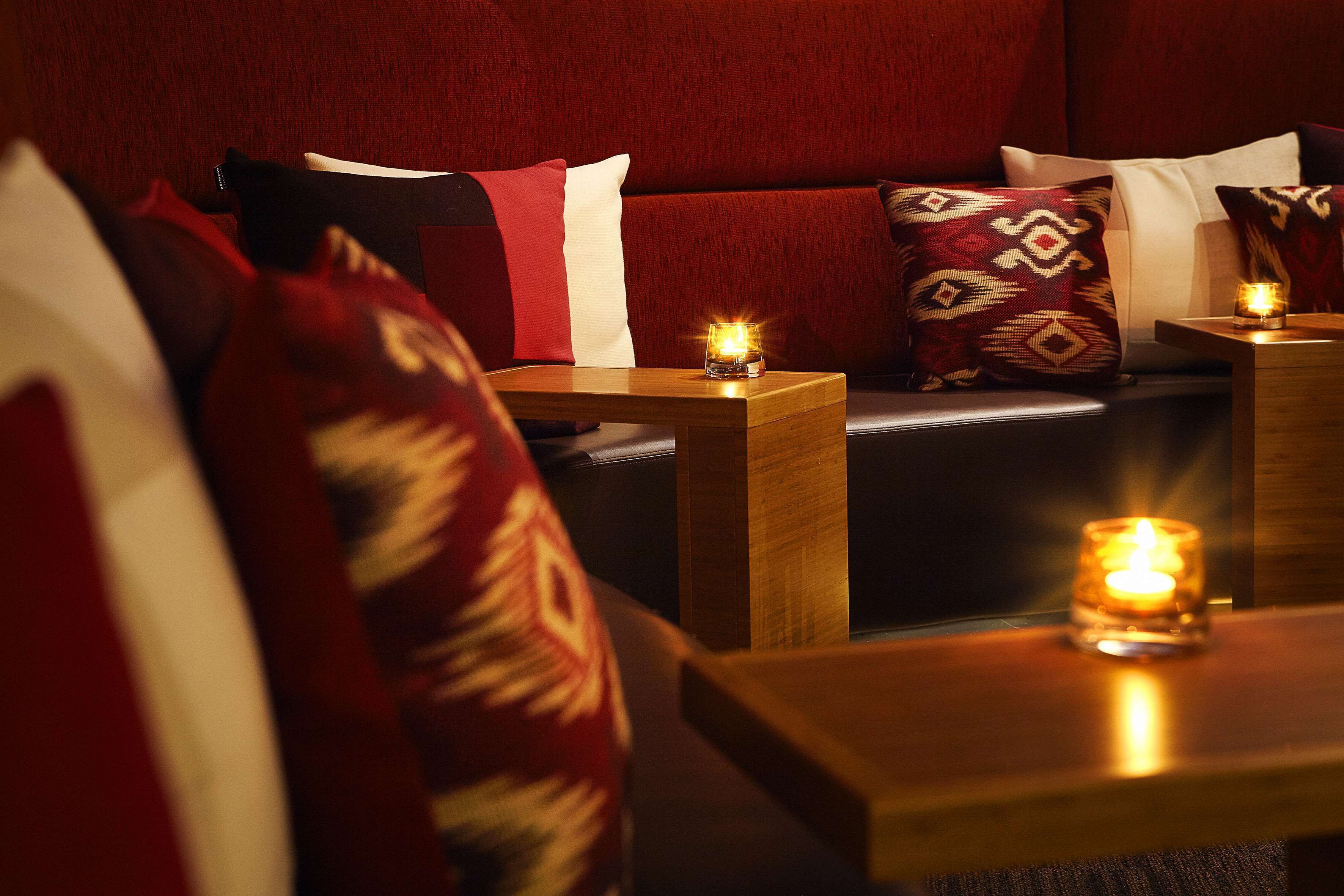 A cozy room with a red sofa, patterned cushions, and two small wooden tables with candles.