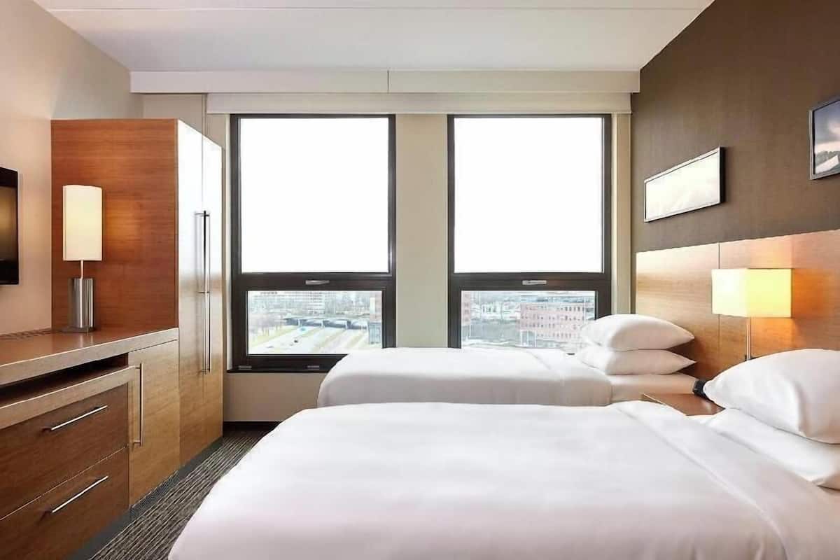 A hotel room with two beds, a desk, a chair, a TV, and a window with a city view.