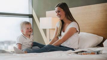 Una mujer y un niño sentados en una cama en una habitación con un ventanal grande y un cabecero de madera.