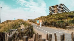 Un chemin menant à un bâtiment doté de nombreux balcons, entouré de dunes herbeuses.