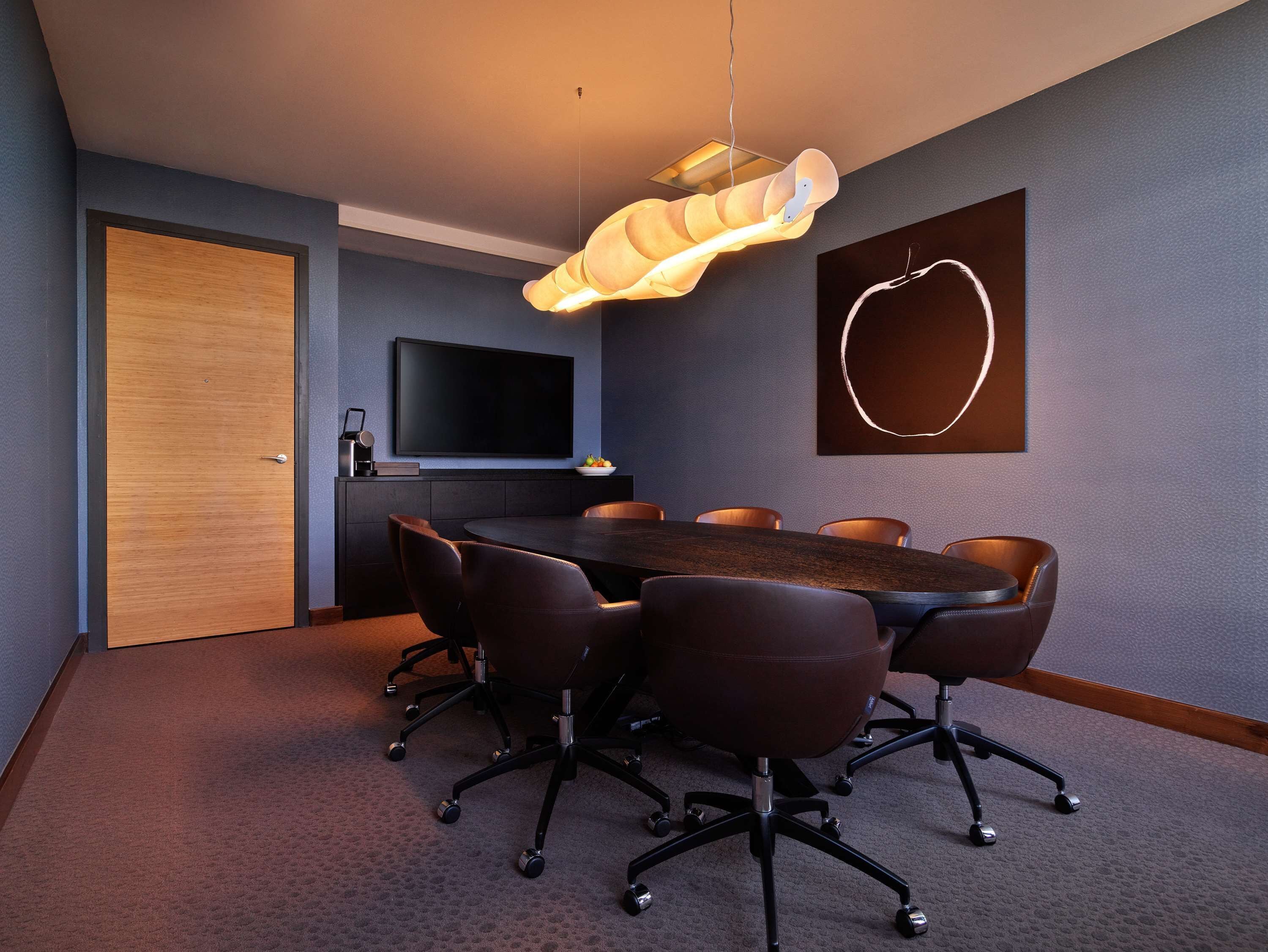 Une salle de conférence équipée d’une grande table, de six chaises, d’un téléviseur à écran plat, d’un luminaire suspendu moderne et d’une œuvre d’art murale.