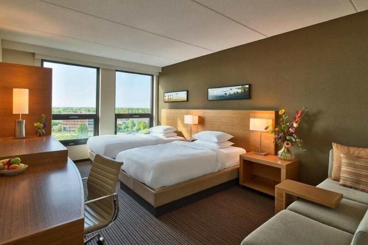 Une chambre d’hôtel avec deux lits, un bureau, une chaise, un canapé et une grande fenêtre donnant sur un paysage agréable.