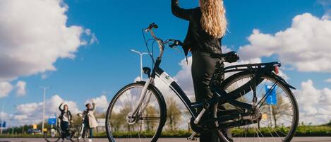 A person standing next to a bicycle on a paved path with a clear sky in the background.