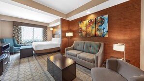 Une chambre d’hôtel avec un lit, un canapé, une table basse, un bureau, une lampe et un tableau au mur.