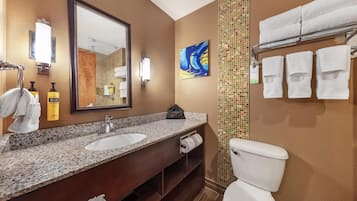 A bathroom with a granite countertop sink, a large mirror, a towel rack, and a toilet.