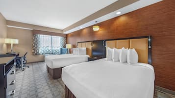 A hotel room with two beds, a desk, a chair, and a window with curtains.