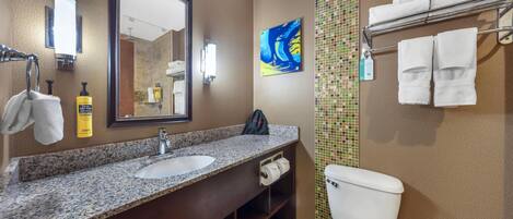 A bathroom with a granite countertop sink, a large mirror, a toilet, and a towel rack with towels.