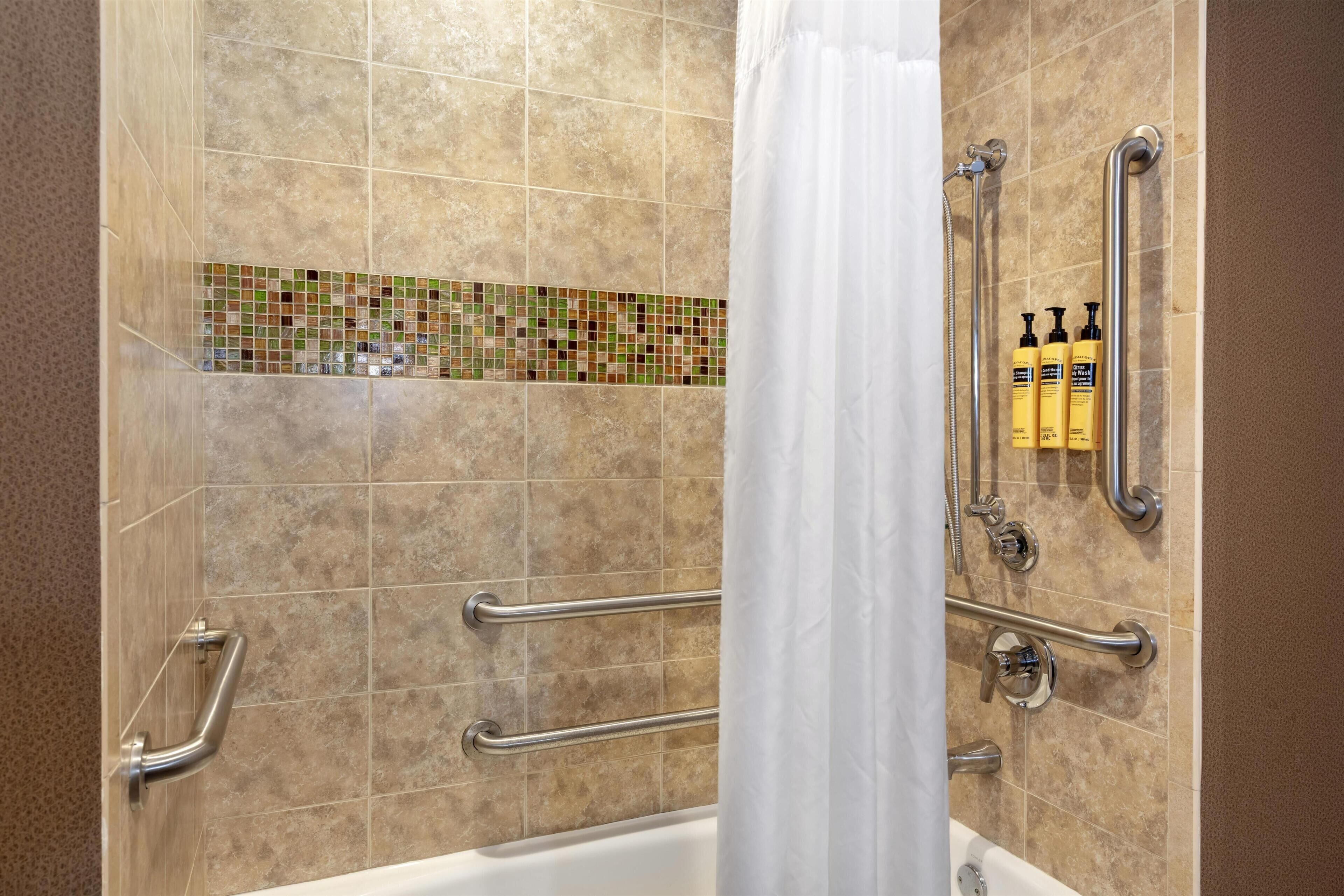 A bathroom with a bathtub, grab bars, a shower curtain, and a tiled backsplash.