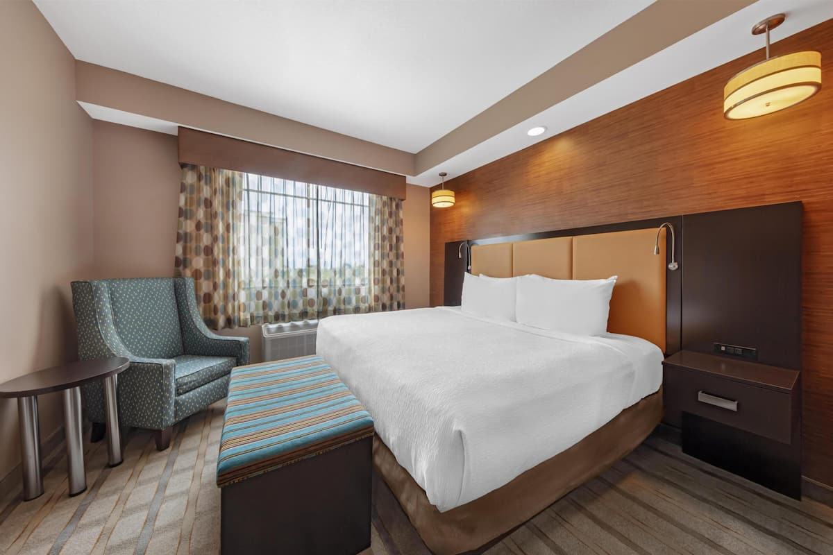 Ein Hotelzimmer mit einem großen Bett, einem Sessel, einem kleinen Tisch und einem Fenster mit Vorhängen.