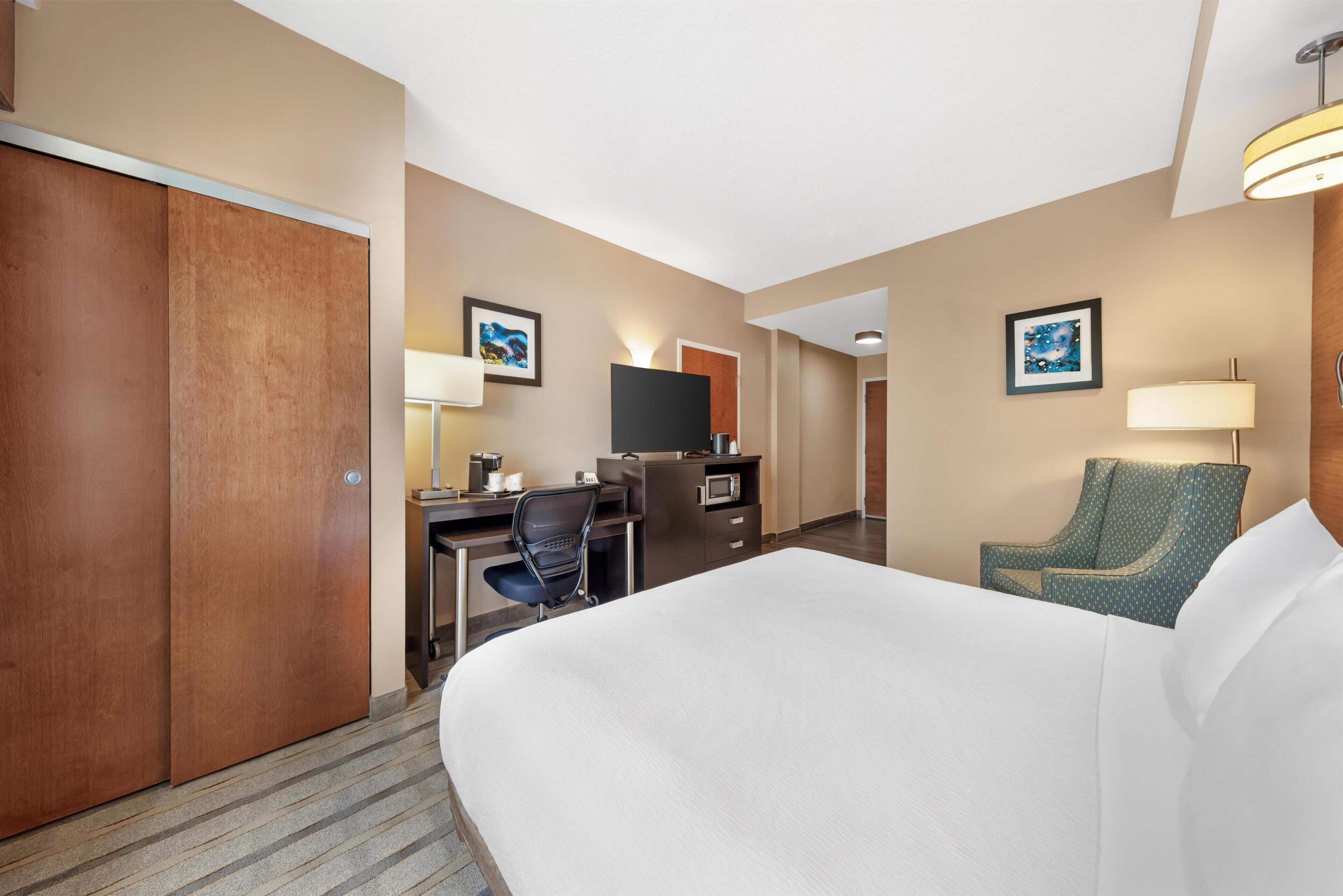 A hotel room with a bed, desk, chair, TV, and artwork on the walls.