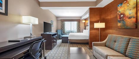A hotel room with a desk, chair, bed, sofa, and artwork on the wall.