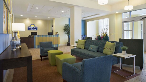 A hotel lobby with a reception desk, seating area with sofas and ottomans, and a large window providing natural light. - Days Inn & Suites by Wyndham Belmont (Belmont)