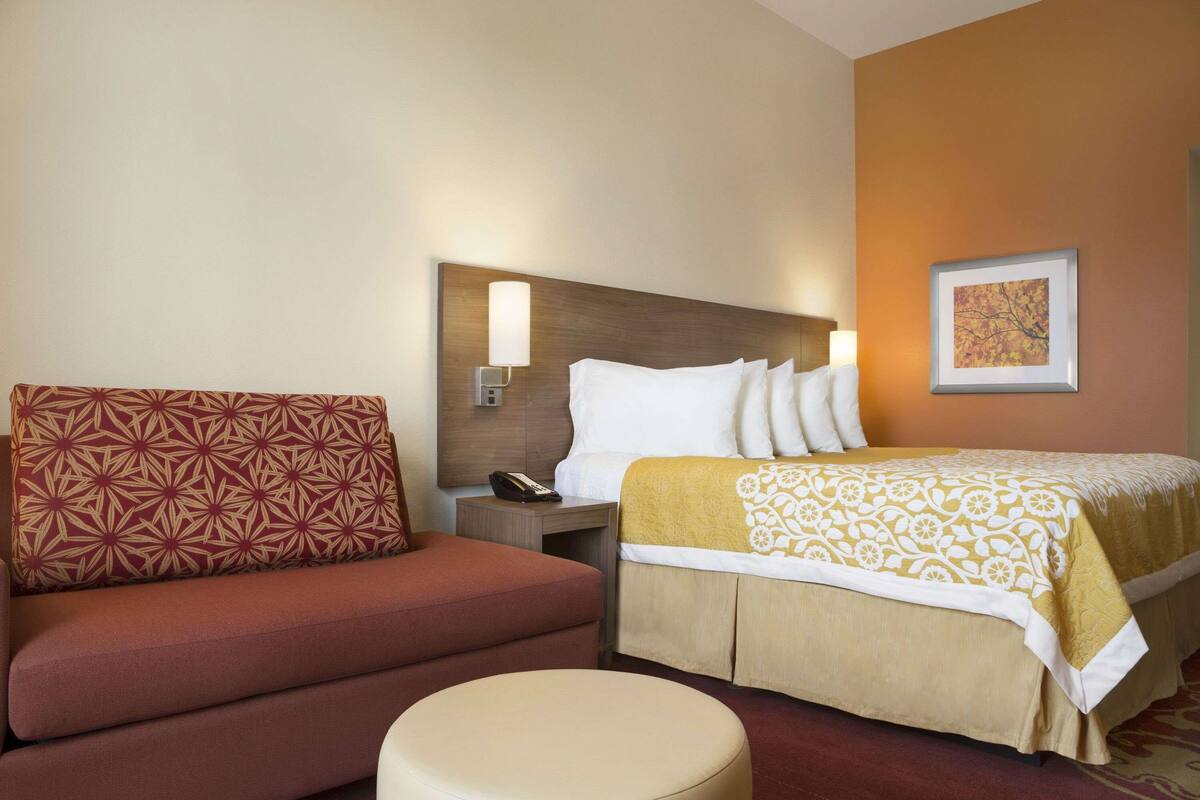Ein Hotelzimmer mit einem Bett, einem Sofa, einem Nachttisch mit Lampe und einem gerahmten Bild an der Wand.