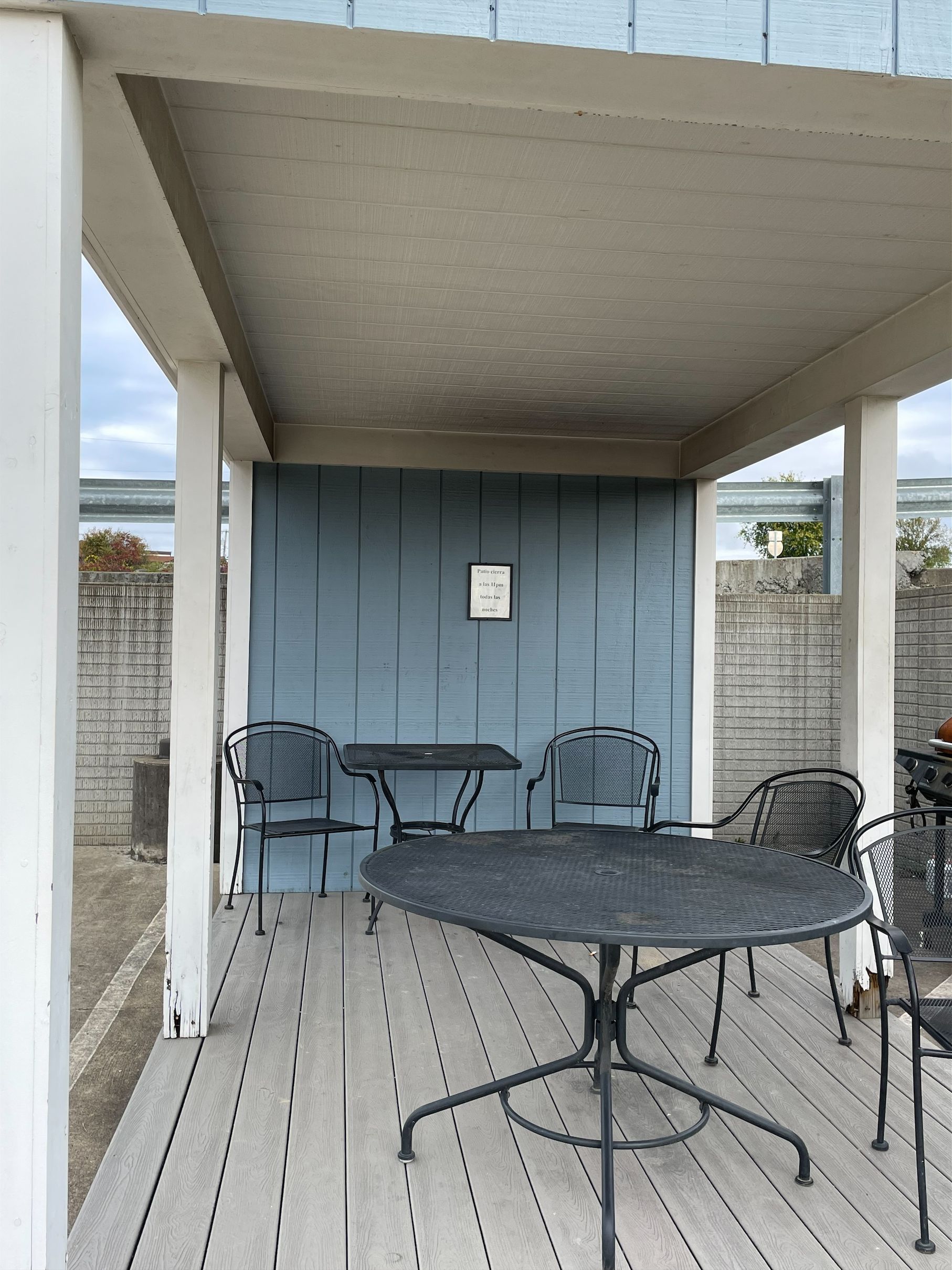 A covered patio with a round table and four chairs, a sign on the wall, and a view of the surrounding area.