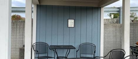 Un patio cubierto con una mesa redonda y cuatro sillas, un cartel en la pared y vistas del entorno.