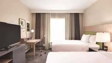 A hotel room with two beds, a desk, a chair, a TV, and a window with curtains.