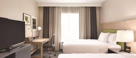 Habitación de hotel con dos camas, un escritorio, una silla, un televisor y una ventana con cortinas.