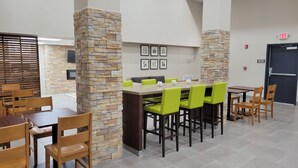 A modern dining area with stone pillars, wooden tables, and green chairs.