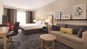 A hotel room with a bed, a sofa, a desk, a chair, a small round table, and framed pictures on the wall.